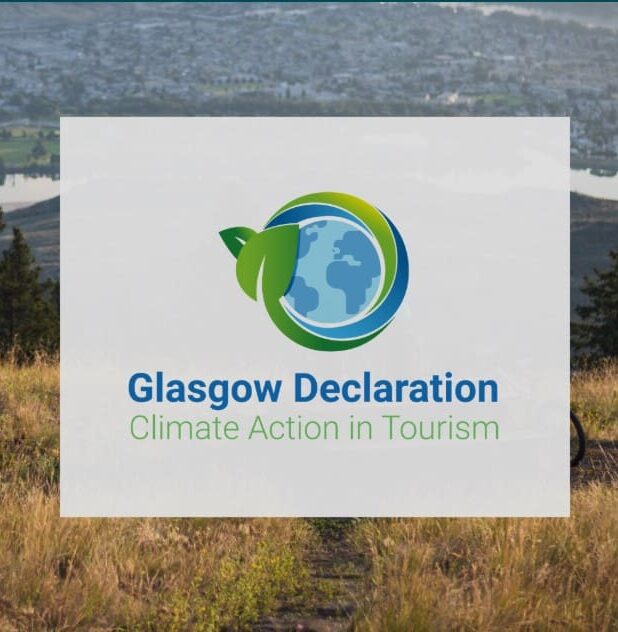 an image of a grass field and a hill, with a white box in the centre, with the logo of the Glasgow Declaration, the planet earth, and the text: Glasgow Declaration Climate Action in Tourism