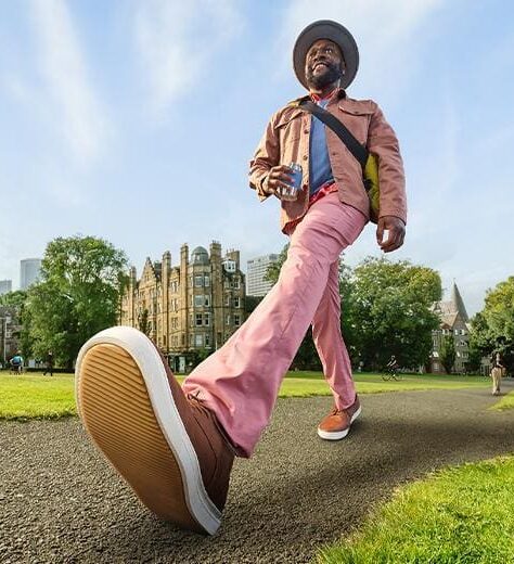 Image of a man, walking on a path in a park, the camera angle is from the ground up, so the foot is a main feature